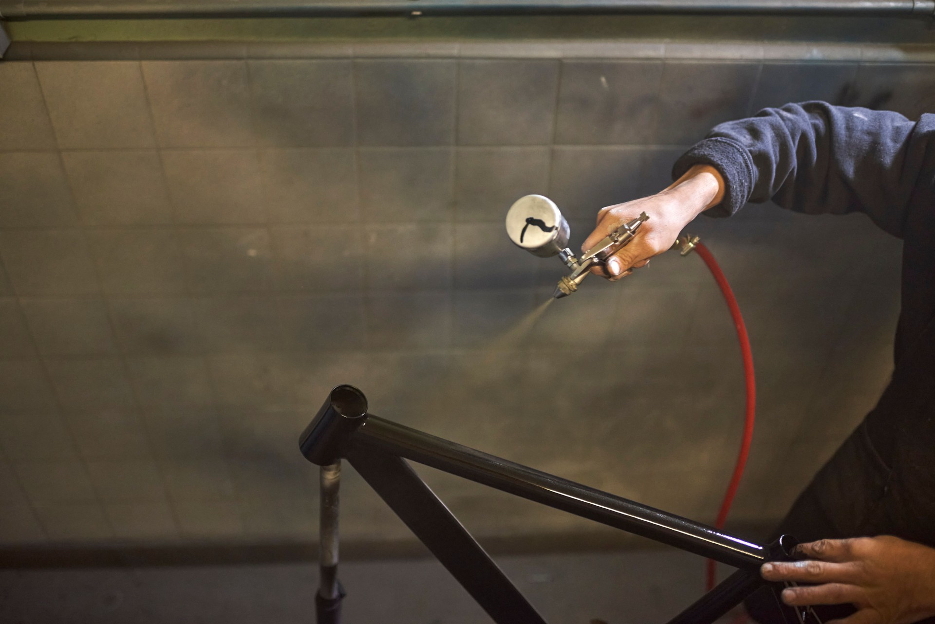 Unrecognizable person spray painting a bicycle frame in his workshop.