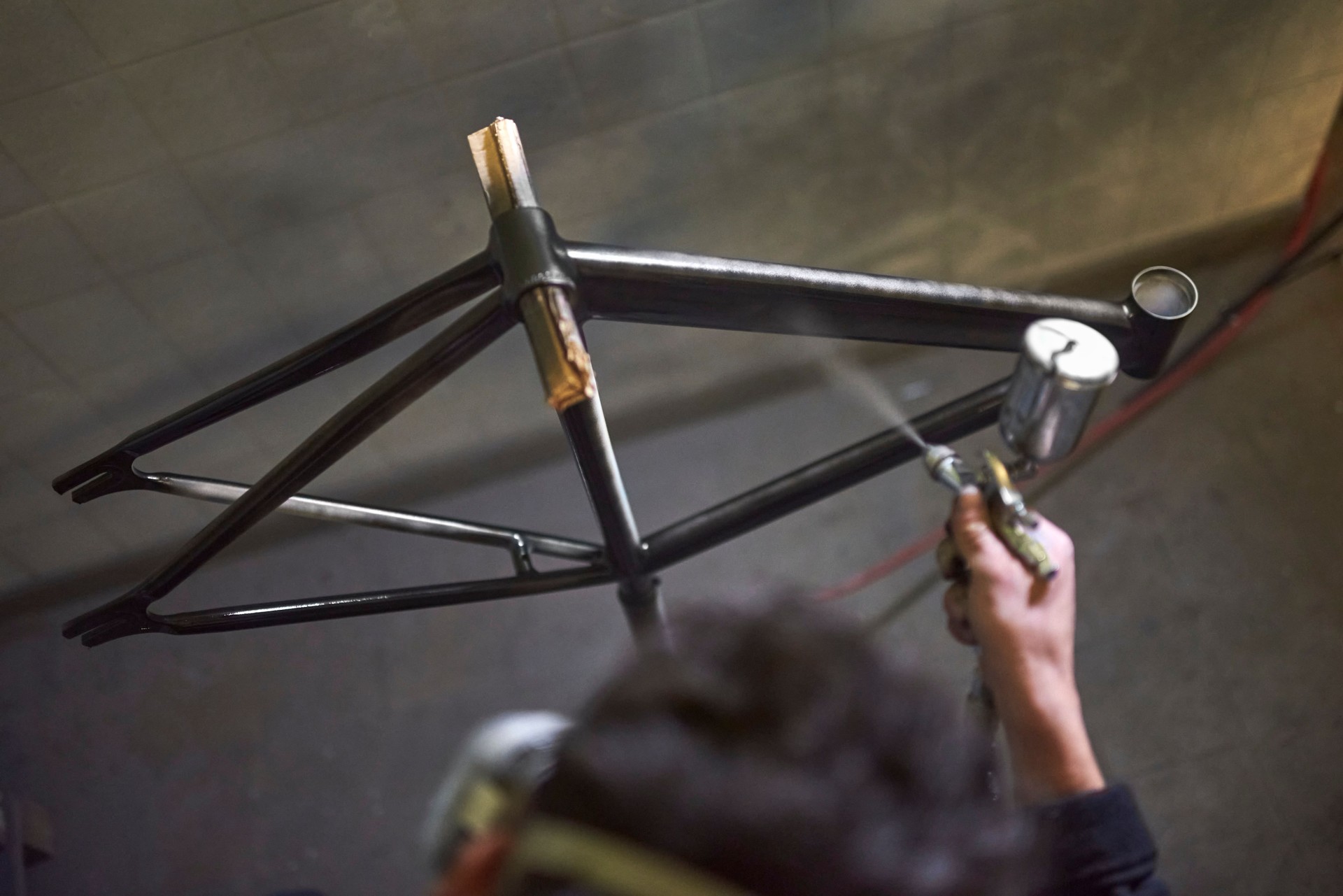Unrecognizable person spray painting a bicycle frame in his workshop.